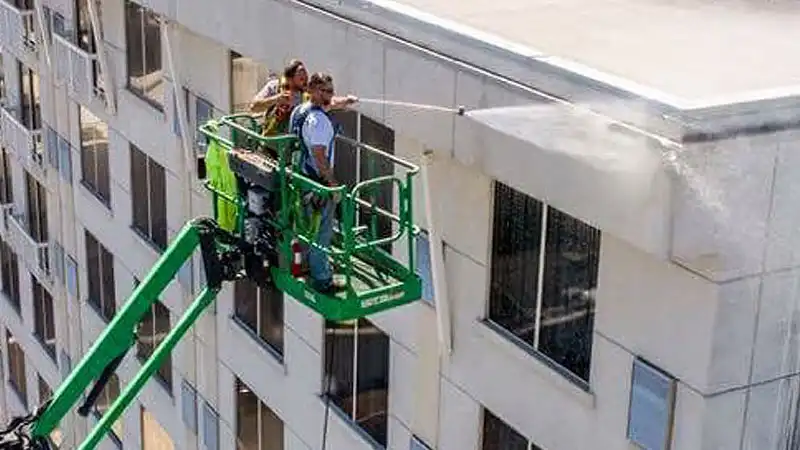 A high-angle drone photo of HurriClean Pressure Washing technicians on a lift soft washing the exterior of 9-story hotel building in the Louisville, KY area.