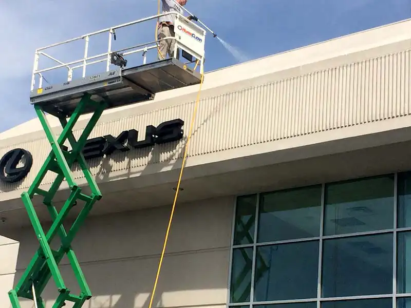 A Hurriclean Pressure washing technician on a scissor lift soft wahed the exterior facade of a car dealership showroom building in the Louisville area.