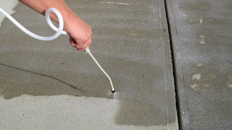 The hand of a HurriClean worker holding a spray wand applies concrete sealer to a commercial retail property's sidewalk in the Lousiville, KY area.