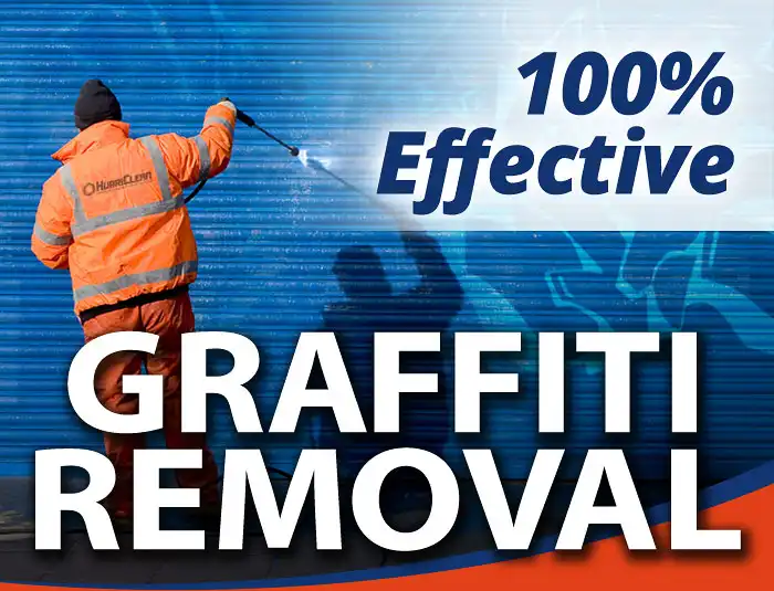 A HurriClean Graffiti Removal Service technician in safety orange cleaning gear pressure washes a blue metal commercial garage door in the Louisville, KY area.