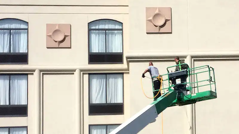 Two HurriClean Pressure Washing technicians on a boom lift Soft Wash the exterior facade of a high-rise multi-unit building in downtown Louisville.