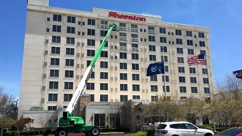 A wide shot of a 9-story high-rise hotel building in downtown Louisville being soft washed by HurriClean Pressure Washing technicians on a boom lift.