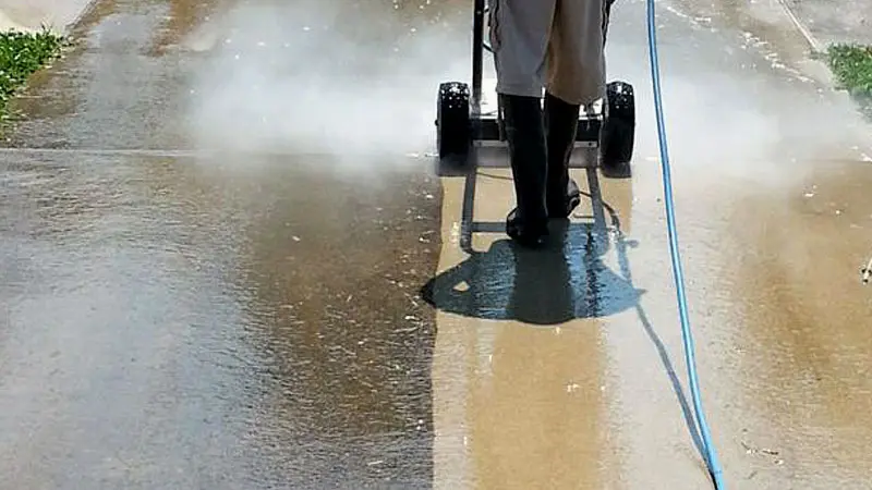 A HurriClean pressure washing technician using a high-pressure surface cleaner on a half dirty and half clean commercial concrete walkway in the Goshen, KY area.