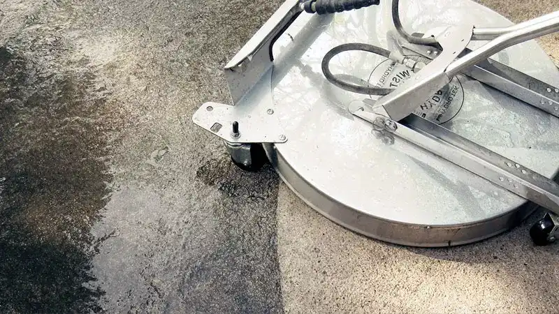 A stainless steel surface cleaner making a clean section on dirty concrete in Goshen, KY to show the deep cleaning power of HurriClean's Driveway Cleaning service.
