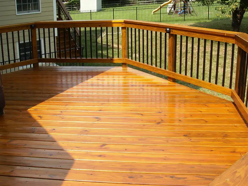 An elevated wooden deck with black railing slats in the La Grange KY area stained and sealed with a glossy golden yellow finish.