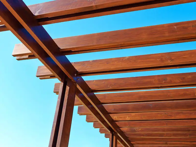 A detailed view of a reddish brown stained wooden pergola with a visible blue sky in the Prospect KY area.
